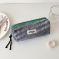 Detailed view of black and white plaid quilted pencil pouch with green zipper and woven label. - Pencil Case / Black