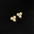 Nahaufnahme von vergoldeten, weissen Emaillblumen-Ohrclips mit filigranen Details. - Doppelschicht-Ohrclips - Weiß Emaille Blume