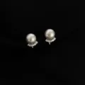Nahaufnahme der eleganten Perlenohrringe mit funkelnden Kristallbogenakzenten auf schwarzem Grund - Zirkonia Glasperle Clip-on / Silber