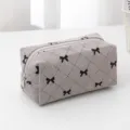 Grey corduroy cosmetic bag detail, featuring black bow embroidery and diamond quilting design. - Gray