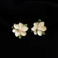 Close-up detail view of elegant white enamel flower earrings with a pearl center and gold trim. - Non-pierced Spiral Clip-on Earrings / Enamel Camellia Style