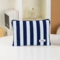 Detailed view of blue white striped cosmetic bag with zipper and logo label on white table. - Blue and White Stripes