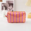 Close-up of pink and orange striped waterproof PVC cosmetic makeup pouch zipper detail. - Striped Orange Purple