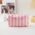 Detailed shot of pink and white striped PVC cosmetic bag on white surface with lifestyle props. - Striped Beige Pink