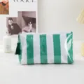 Close-up detail view of the green and white striped PVC cosmetic bag with a cute tassel zipper pull. - Small Green White