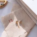 Detailaufnahme von minimalistischen Goldkugel-Ohrringen auf strukturiertem Leinenstoff. - Runder Kugelstift (A66)