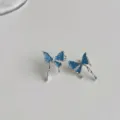Close-up of blue dripping butterfly silver stud earrings, delicate minimalist detail jewelry. - Blue