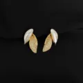 Nahaufnahme goldener Ohrringe mit Zirkonia und weißem Emaille auf schwarzem Stoff. - Zirkonia Blatt