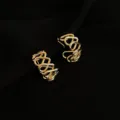 Nahaufnahme von kunstvollen vergoldeten geometrischen Clip-Ohrringen mit gedrehtem Design. - Hohle Große Creolen