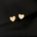 Nahaufnahme Detail goldener Herz Ohrringe mit weißem Perlmutt Inlay und strukturierter Kante. - Muschel und Herz Stil