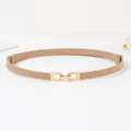 Détail de la fine ceinture pour femme avec boucle dorée minimaliste et lanière couleur kaki. - Beige