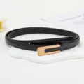 Gros plan sur la fine ceinture en cuir noir pour femme avec élégante boucle dorée sur support. - 1,4 cm de large, 105 cm de long / Noir