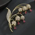 Exquisita broche de lirio de los valles chapada en oro con circonitas brillantes y dijes rosas. - Rosa