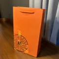 Close-up view of a vibrant orange paper gift bag featuring a unique black circular motif. - Orange Classical Plum Blossom Carry Box