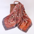 Detailed view of orange silk paisley scarf draped on luxury leather bag background elegance. - 90cm / Paisley Red-Orange
