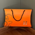 Orange pillow gift box with black handle and chain design, elegant packaging for scarves and gifts. - Orange Ingot-Shaped Jewelry Box