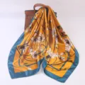 Detail view of a 90cm silk square scarf in golden yellow with blue border and floral print. - Orange Magnolia