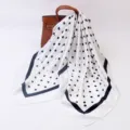 Detailed view of elegant black and white polka dot square silk scarf draped on a bag. - White Polka Dot