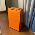 Orange paper gift bag with black borders and handles for scarves and apparel packaging. - Premium Scarf Orange Carry Box