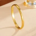 Close-up detail shot of a sleek gold-colored plain metal bangle bracelet on a textured surface. - 4mm Gold Plain Circle Bangle (G315) / Gold