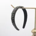 Vue détaillée du serre-tête en strass noirs, cristaux scintillants et griffes dorées élégantes. - Noir