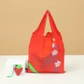 Foldable red reusable shopping bag with cute strawberry storage pouch and floral patterns. - Strawberry Red