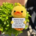 Detailed shot of handmade crochet cute yellow duck holding positive message encouragement card. - Duck