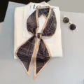Detailed view of the elegant geometric pattern skinny scarf styled on a white blazer. - Style 29