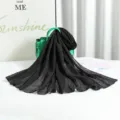 Detailed view of the black pleated shimmering scarf draped over a green handbag in studio scene. - Silver Wire Black