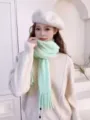 Detailed shot of a soft mint green fuzzy tassel knit scarf worn with a chic sweater and beret. - Light Green