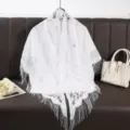 Close-up detail of white lace fringe shawl with hollow floral pattern, elegant and breathable. - White