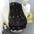 Black metallic monogram scarf detail, draped on a stylish white rattan chair for autumn fashion. - Black