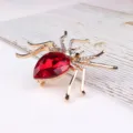 Close-up view of a stunning spider brooch detailed with a red teardrop crystal and clear rhinestones. - Gold + Light Bright Red