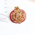 Detailed closeup shot of a red enamel pomegranate brooch adorned with sparkling amber crystals. - Watermelon red