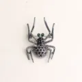 Detailed shot of a stylish black spider brooch with sparkling rhinestones and green crystal eyes. - Gun Black