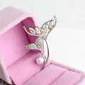 Detailed view of a stunning rhinestone and pearl fish tail brooch in a pink velvet box. - Silver and White AB