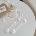 Detailansicht weißer transparenter Socken mit schönen Schleifen auf dem weißen Tisch. - Einheitsgröße / Weiß