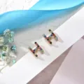 Close-up detail of colorful rhinestone letter H stud earrings on white card with blue ribbon. - Letter H