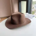 Detail view of a brown western cowboy straw hat featuring rolled brim on white table. - Coffee