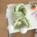 Green knit scarf detail showing soft wool texture, cute white pom pom and decorative label. - Green