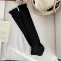 Black knitted stirrup leg warmers with ruffle trim, cozy winter fashion accessory. - Black