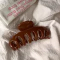 Detailed close-up view of a glossy brown plastic hair claw clip on a white fabric surface. - Round Head Dragon Bone / Large Style / Caramel color