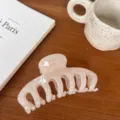 Detailed view of a elegant light pink resin hair claw clip resting on a warm wooden table. - Round Head Dragon Bone / Large Style / Jelly White