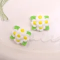 Gros plan de breloques de fleurs en résine blanche avec feuilles vertes et cœurs jaunes. - Blanc