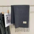 Detail view of a cozy dark grey reversible cashmere feel scarf with fringe hem texture. - Black and Gray