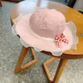 Close-up detail of a cute pink children sun hat with pearl lace trim and checkered bow. - 54cm / Pink
