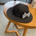 Detail view of black children sun hat featuring chic houndstooth bow accent on wooden table. - Black Houndstooth Bowknot