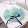 Detail view of a light green straw sun hat with navy blue bow ribbon on white table. - Aqua Green