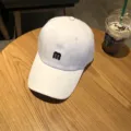 White baseball cap with black embroidered letter M. Classic curved brim sun hat for daily wear. - Adjustable / White