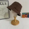 Detailed view of the brown pleated bucket hat on a wooden mannequin head display stand. - M (56-58cm) / Coffee